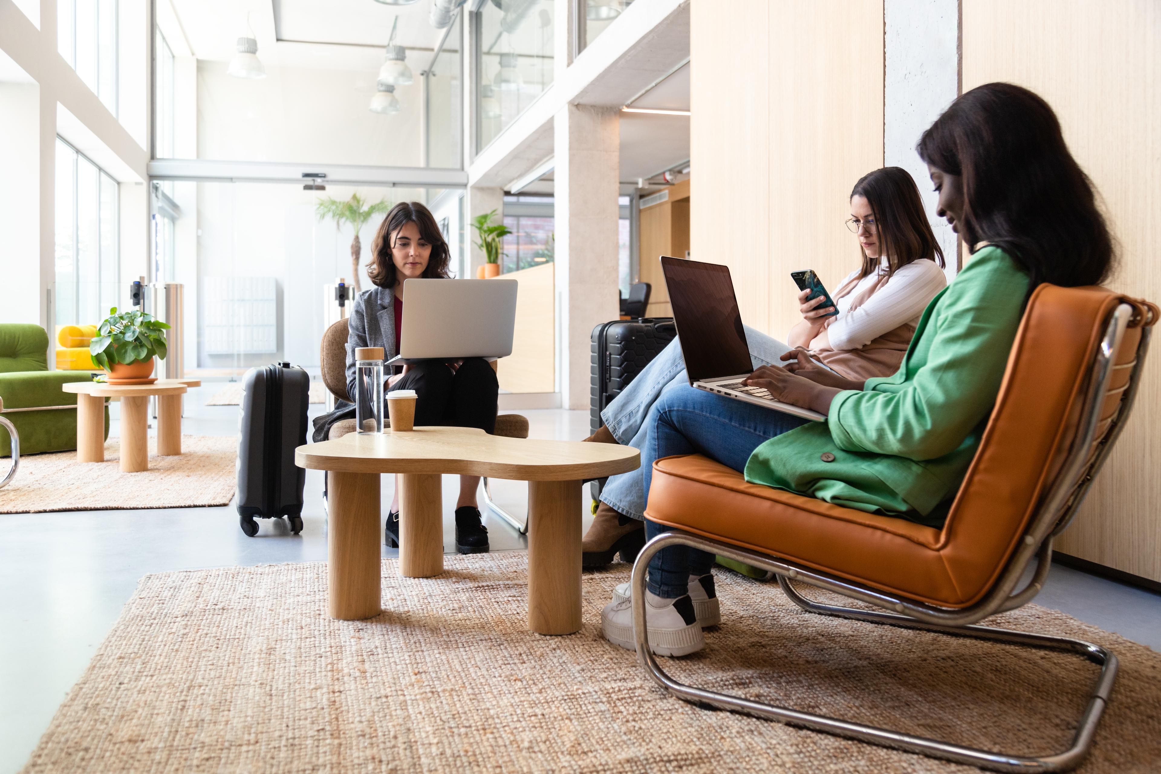 group of people sitting in lounge with laptops and phones